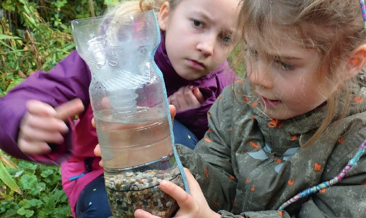 Zwei Mädchen experimentieren mit einer Wasserflasche in der Natur